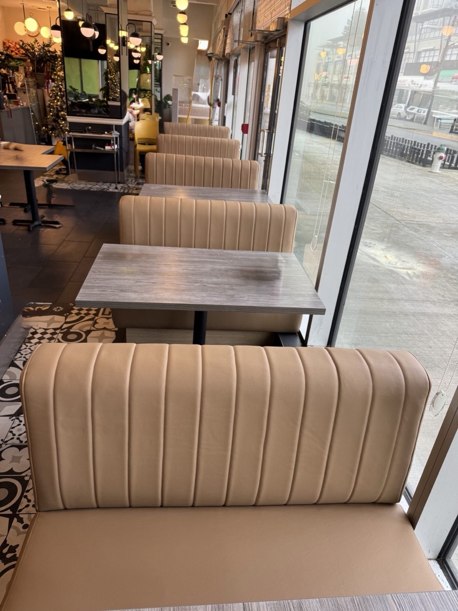 Beige channel-tufted booth backs with grey stone tables in a cafe by street windows