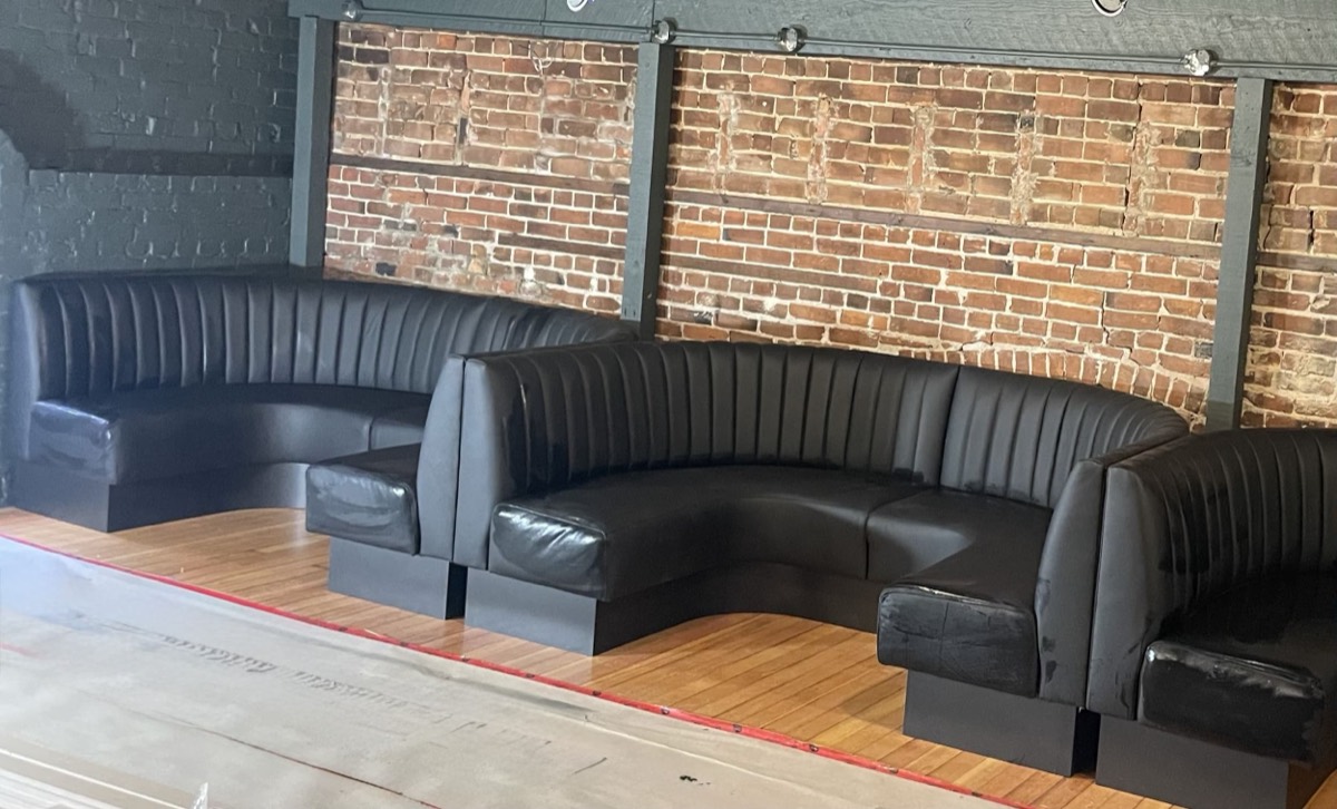 Black channel-tufted booths and a curved unit lined up against an exposed brick wall