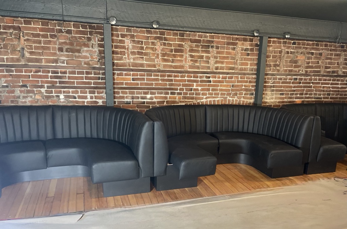 Black channel-tufted curved booth seating against an exposed brick wall