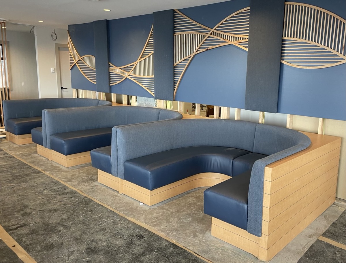 Blue vinyl curved and straight booths with pale wood bases against blue walls with slatted art