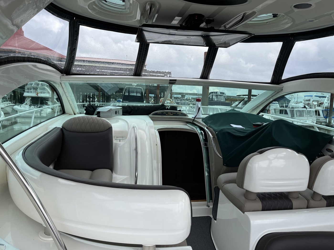 Boat cockpit with white and grey vinyl helm seats under a clear canvas enclosure