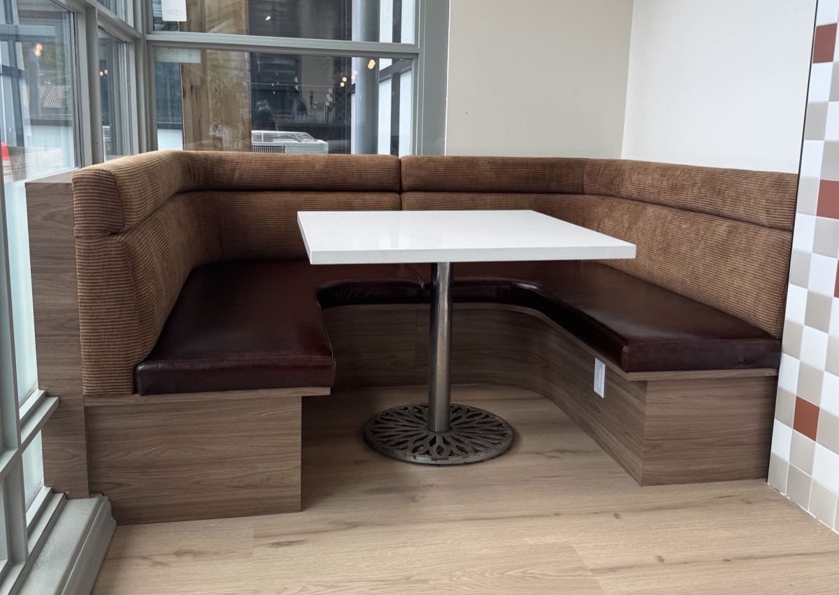 Corner booth with a ribbed brown backrest, dark burgundy seat cushions and a white table on a wood base