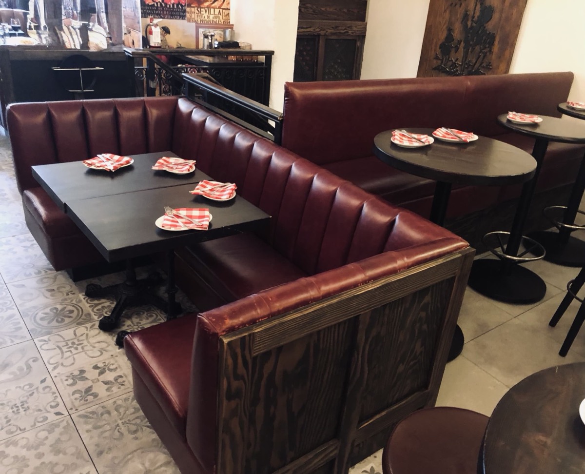 Burgundy channel-tufted booths with wood back panels and black tables on patterned tile