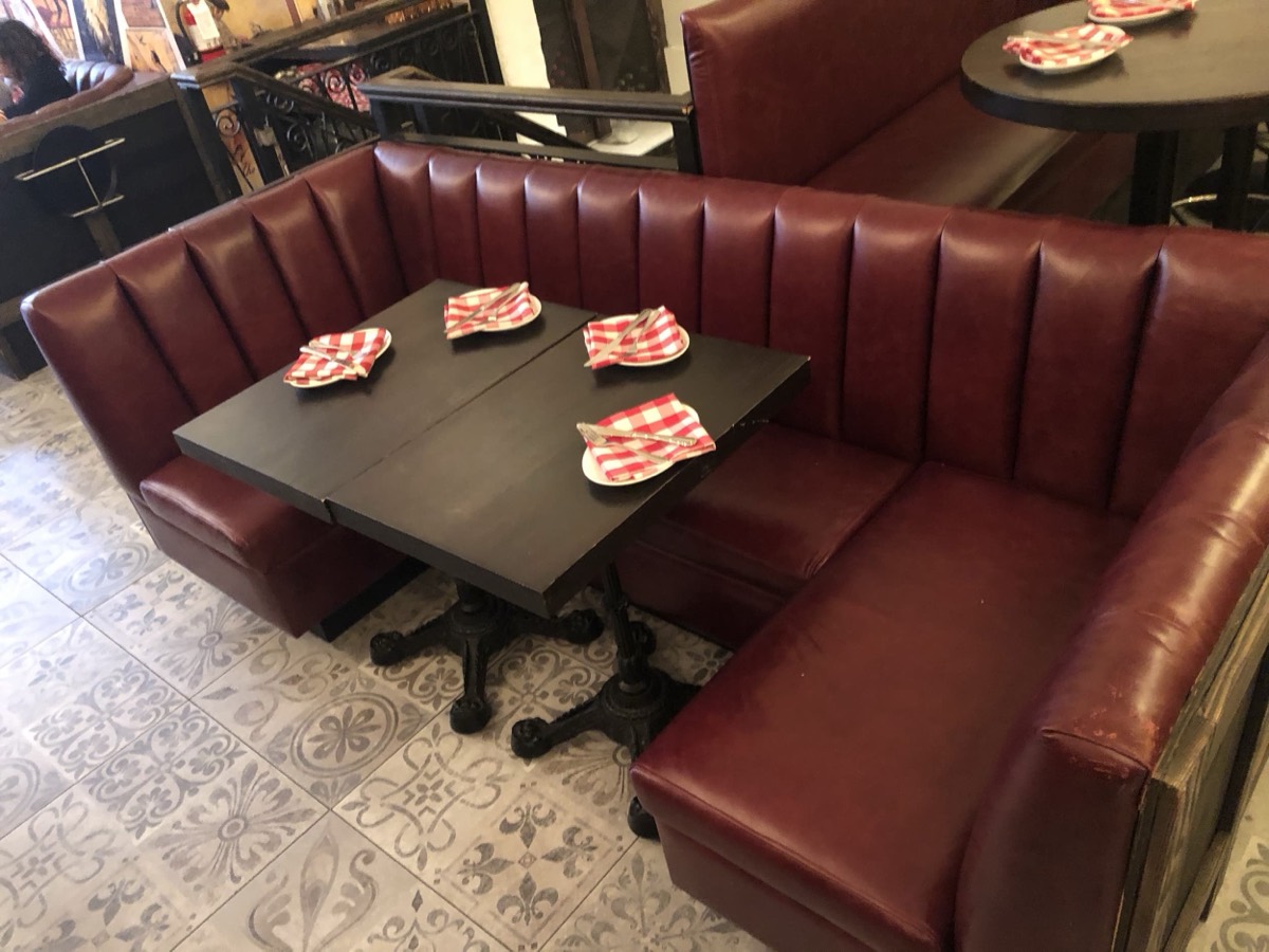 Burgundy channel-tufted corner booth with black tables and red checked napkins on patterned tile