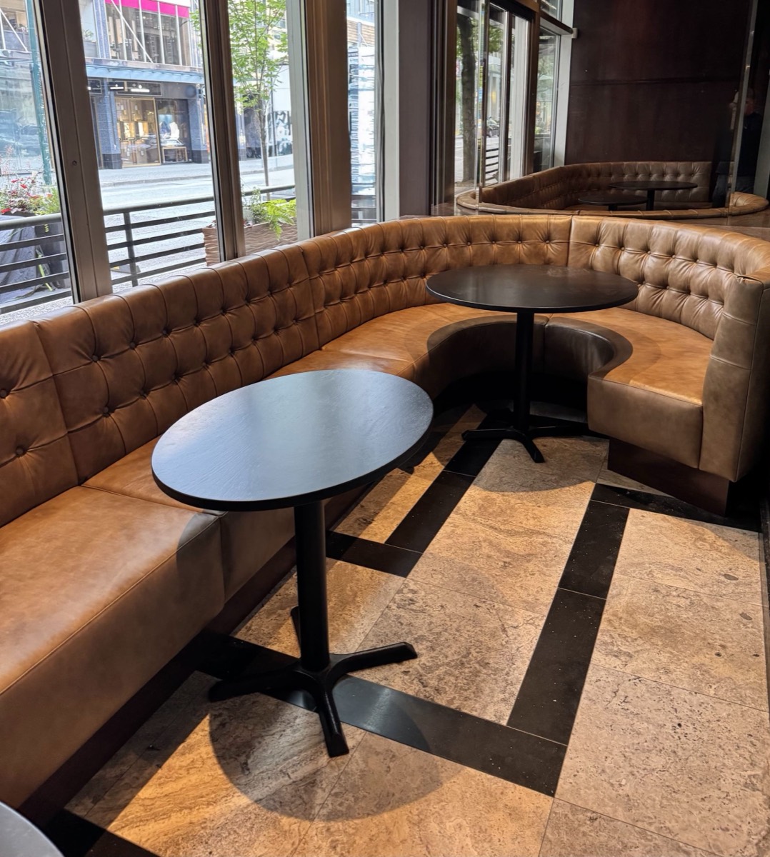 Caramel diamond-tufted banquettes and a curved booth with black tables beside large street facing windows