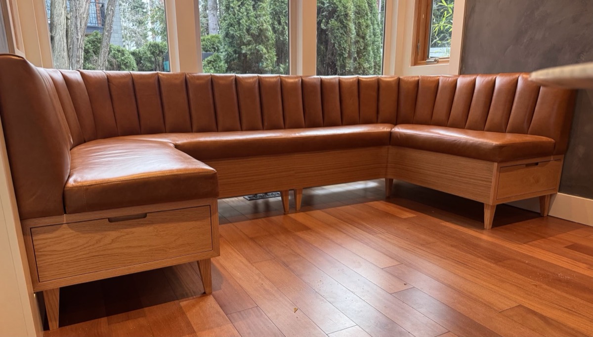Cognac leather channel-tufted corner banquette on an oak base with storage drawers by windows