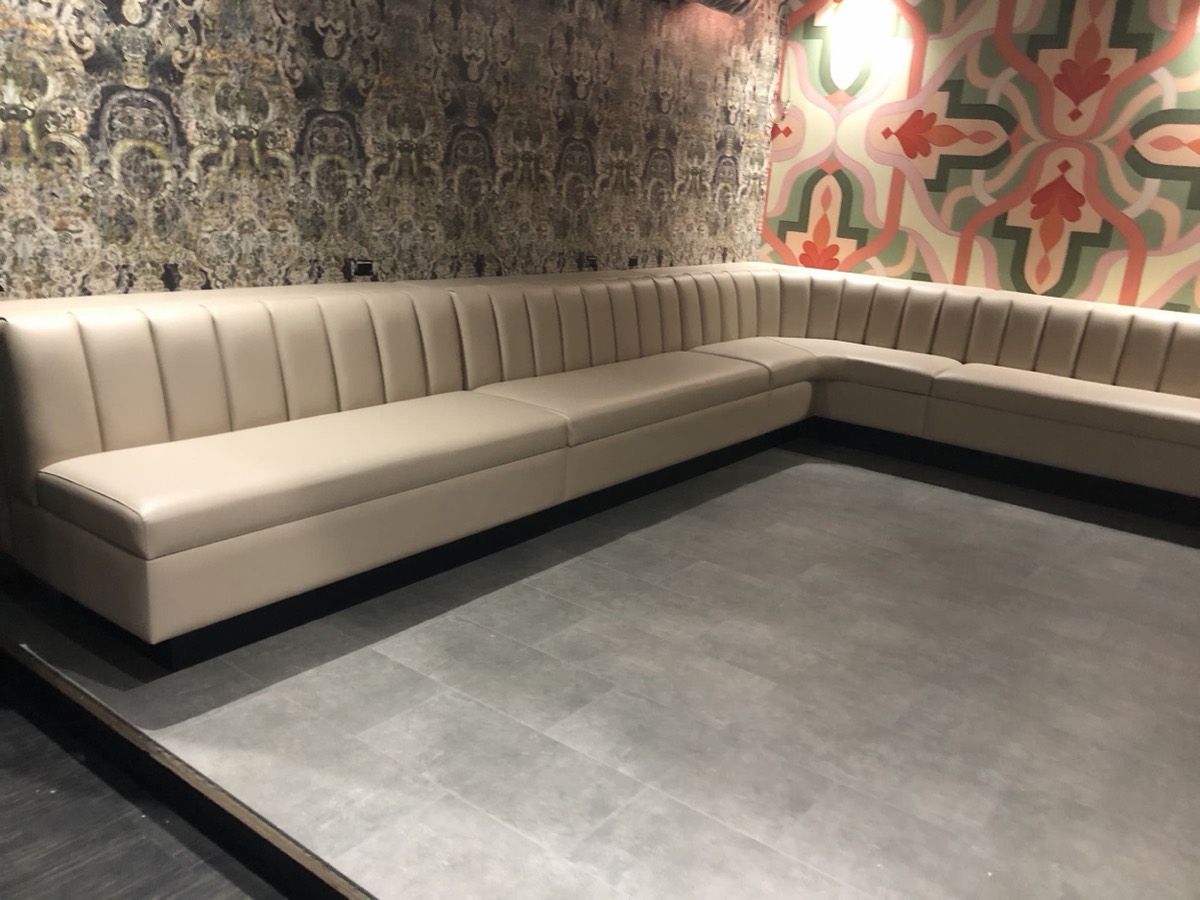 Cream channel-tufted corner banquette against patterned wallpaper with grey tile flooring