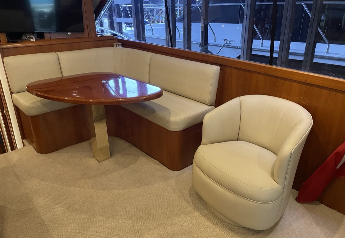 Yacht interior dinette with a cream leather L-shaped settee, wood table and matching swivel tub chair