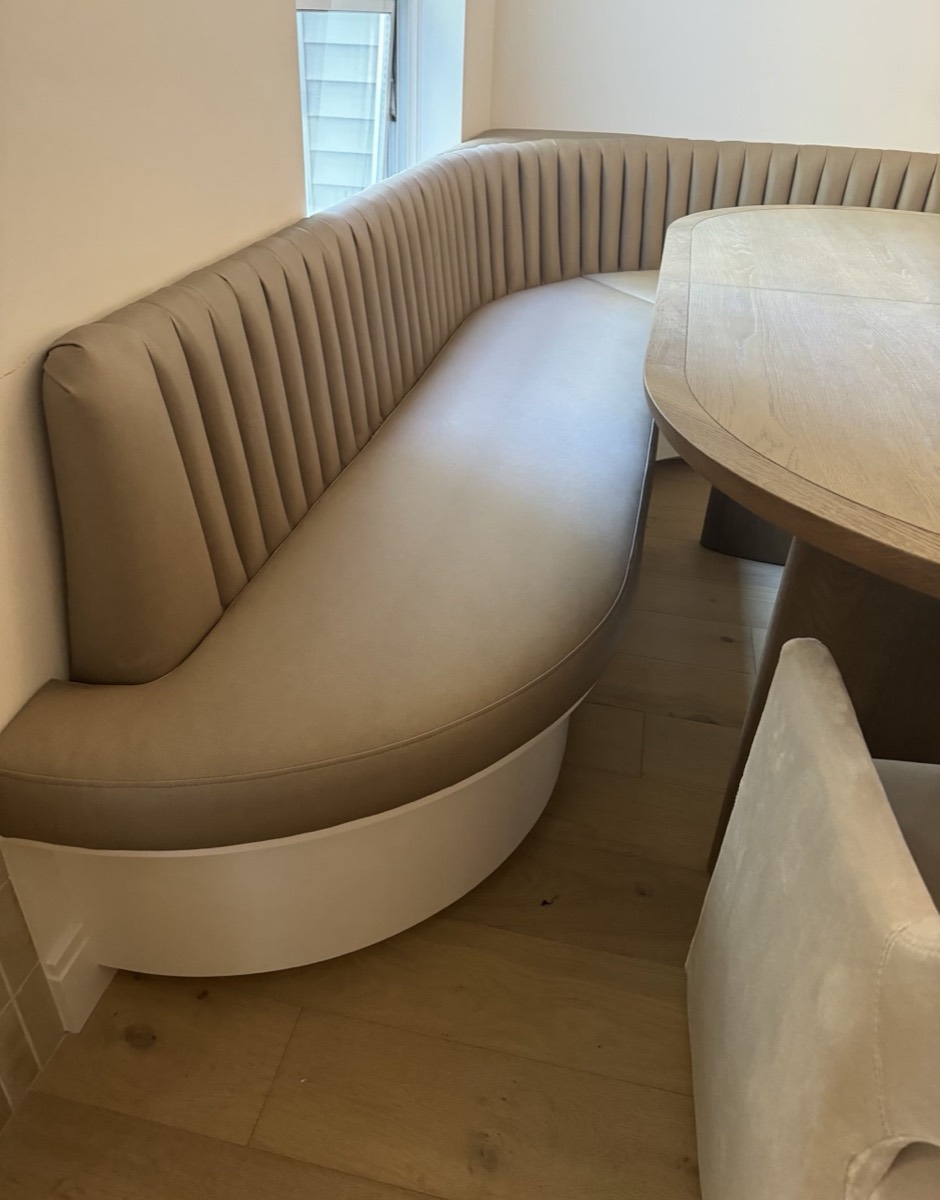 Curved greige channel-tufted banquette with a white plinth base wrapping an oval dining table