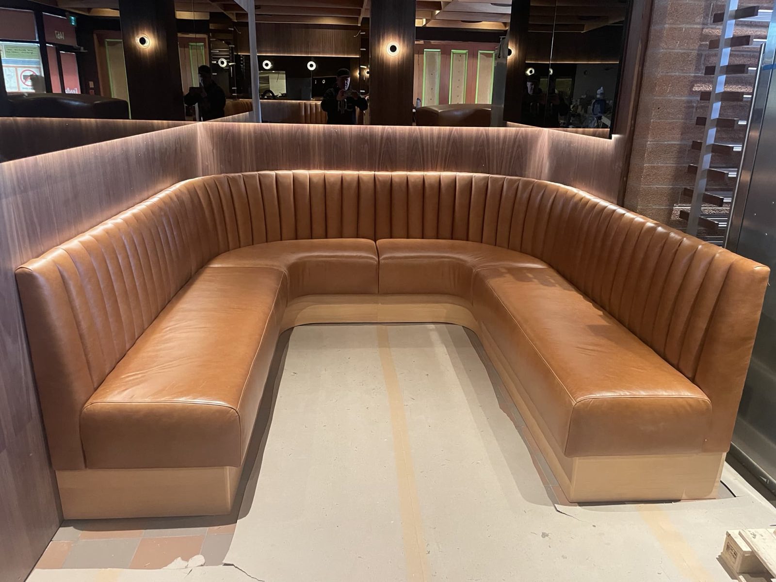 Finished curved caramel leather booth in an upscale restaurant with wood panelling and mirrors