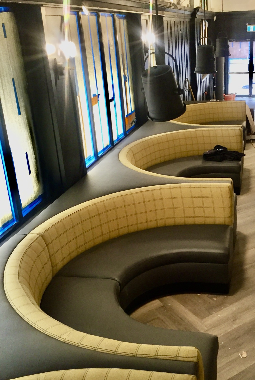Curved plaid fabric booth seating on a black leather base under pendant lighting