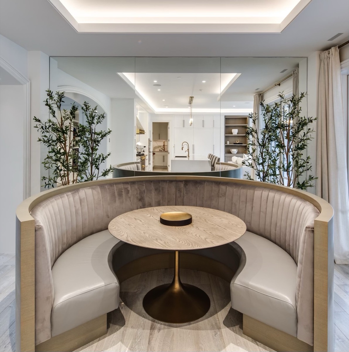Curved taupe velvet banquette with cream seats around a round oak table