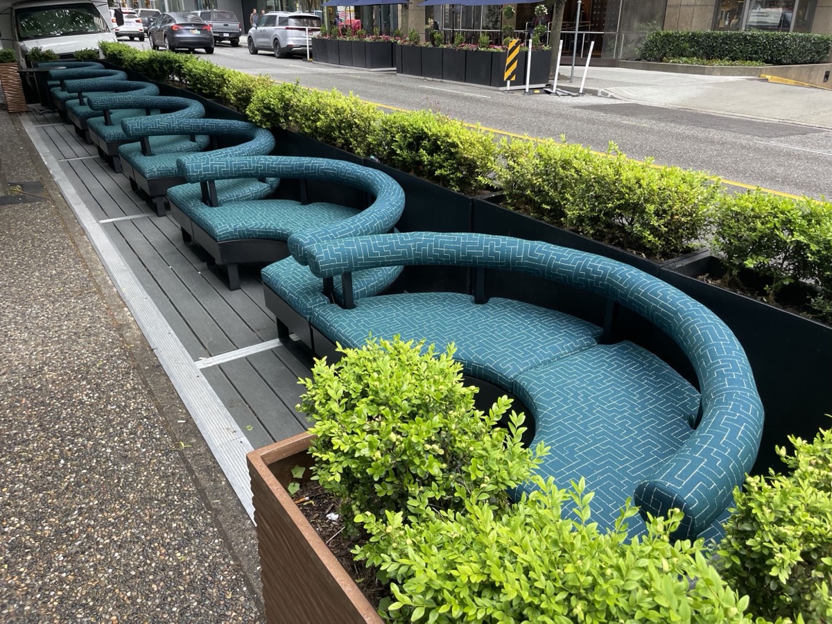 Row of curved teal patterned banquettes along a sidewalk parklet with hedge planters