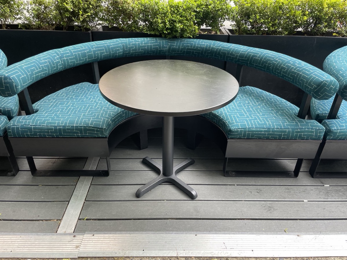 Curved teal patterned outdoor banquette with a round black table on a wood deck