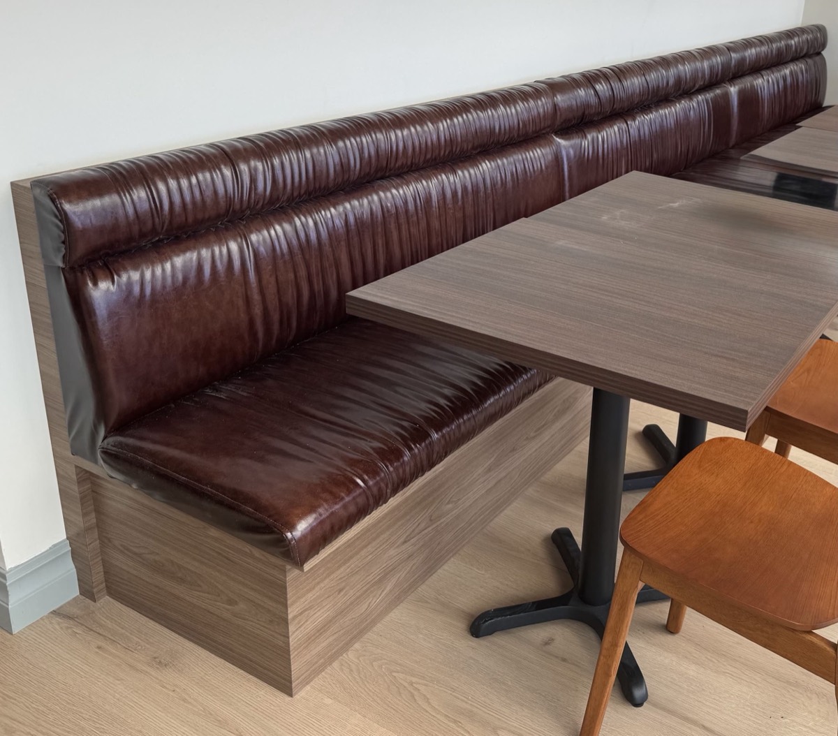Glossy dark brown channel-tufted banquette with a wood plinth base beside wood dining tables