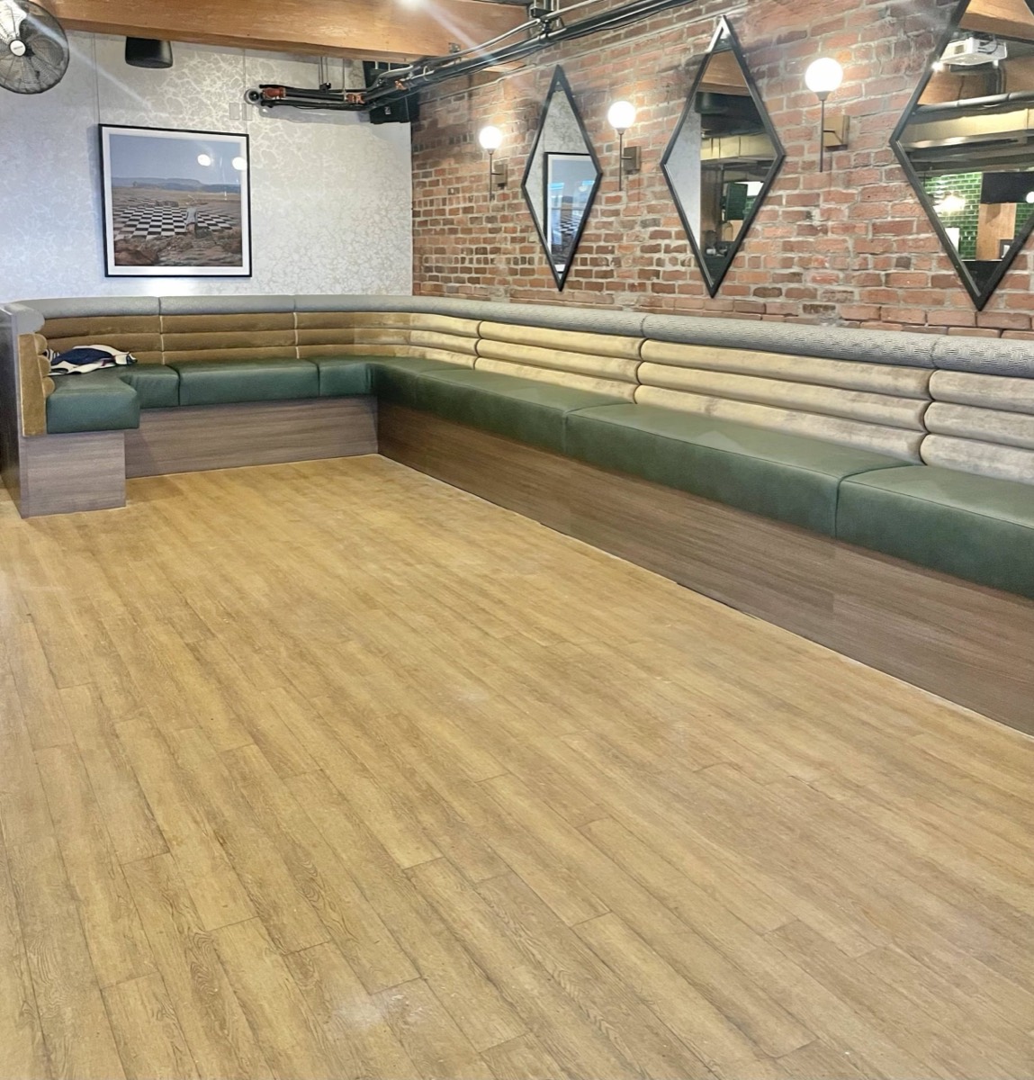 L-shaped bench with horizontal green and cream padded rolls under diamond mirrors on a brick wall