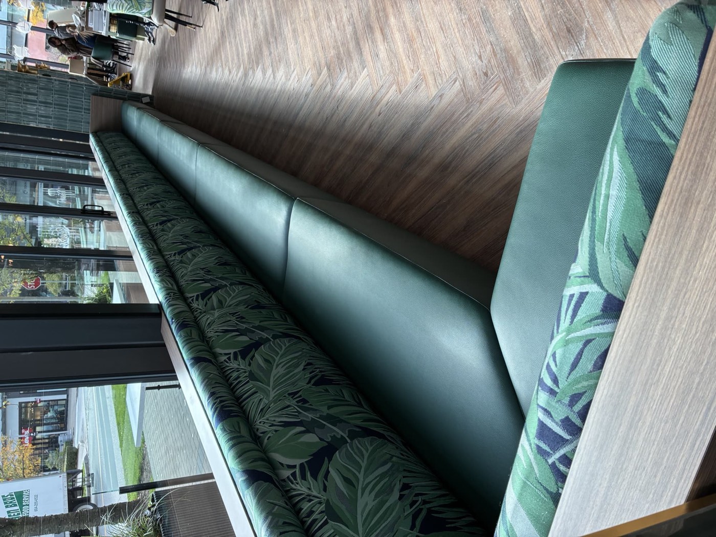 Long green vinyl banquette bench with tropical palm print back cushions beside cafe storefront windows