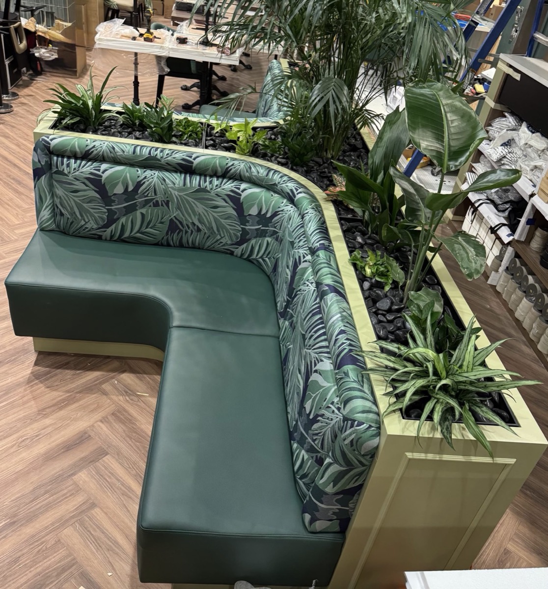 L-shaped green vinyl banquette with palm print backrest built into a live planter divider