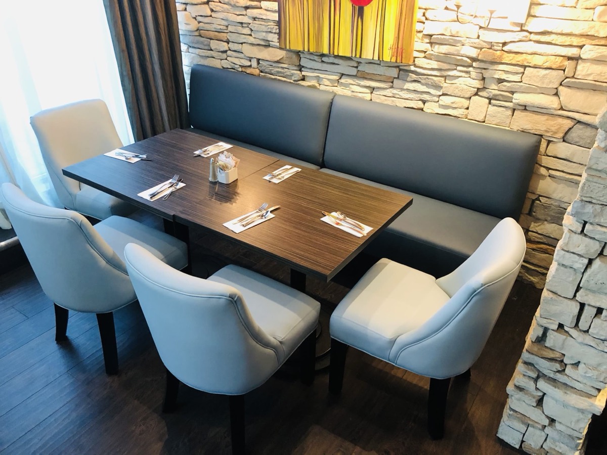 Grey bench seating against a stacked stone wall with a walnut table and cream tub chairs