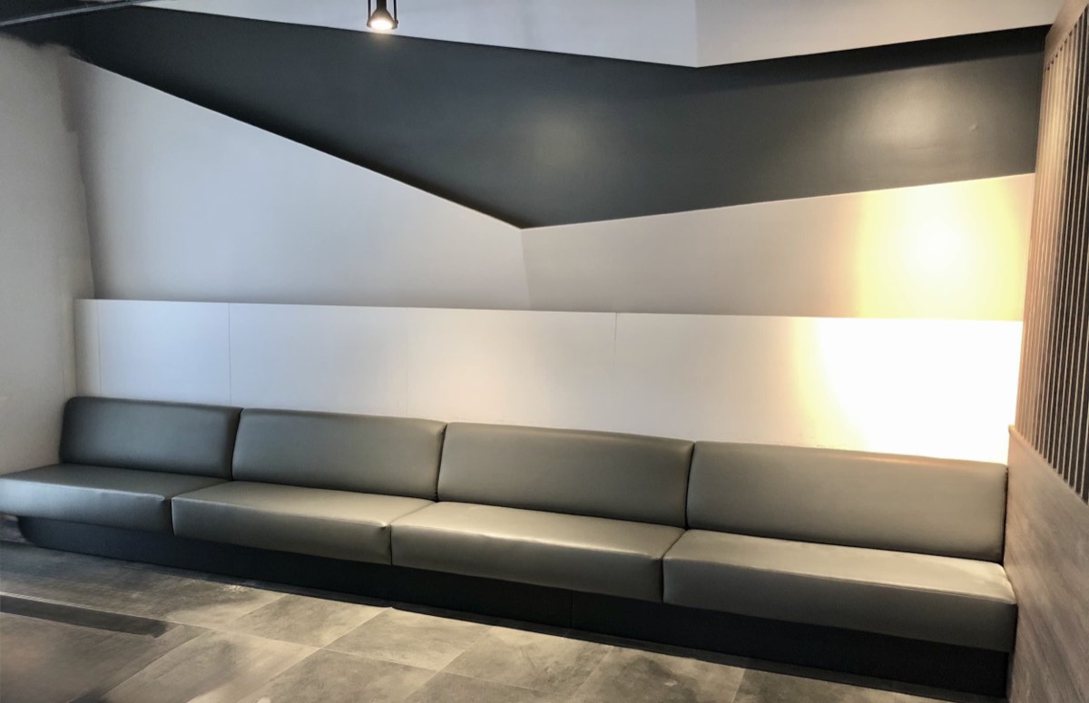 Long grey leather wall bench with an angled dark ceiling and backlit panel in a modern lounge