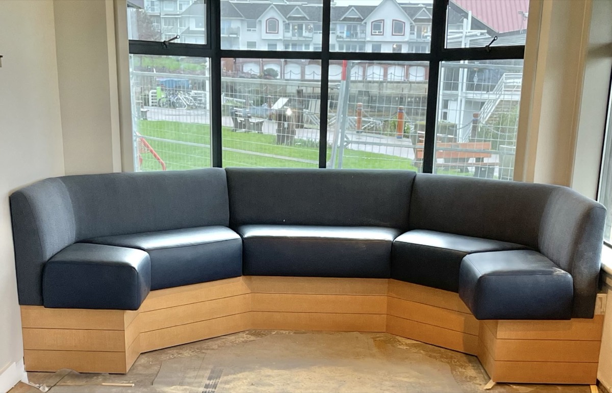 Navy upholstered curved banquette on a wood base beside a window in a hospitality lounge