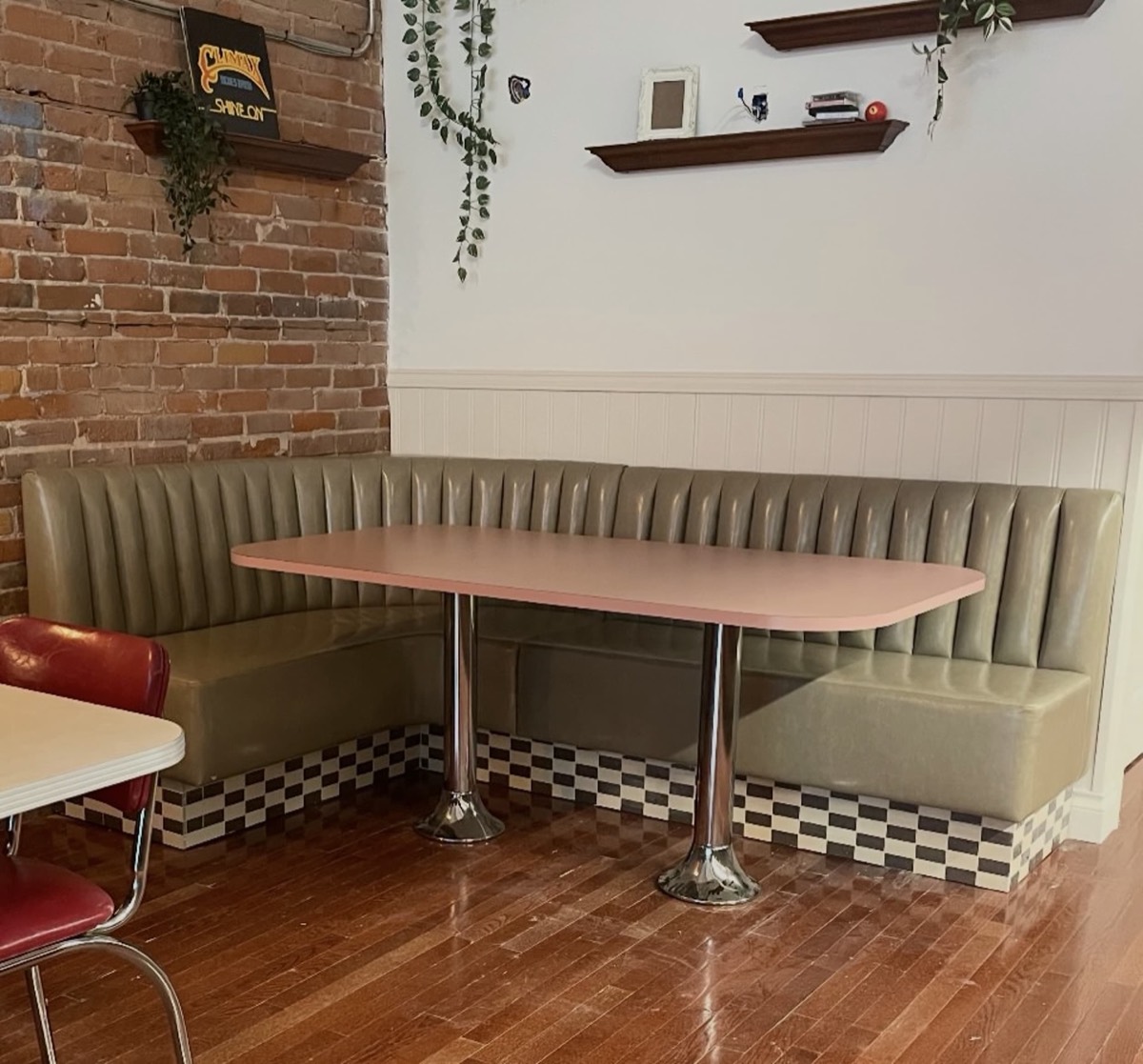 Olive green channel-tufted banquette in a retro diner with exposed brick and a pink table top