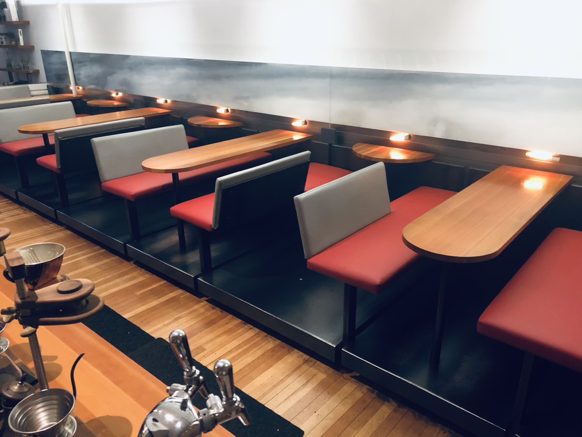 Red and grey bench booths with rounded wood tables in a bar seen past the beer taps
