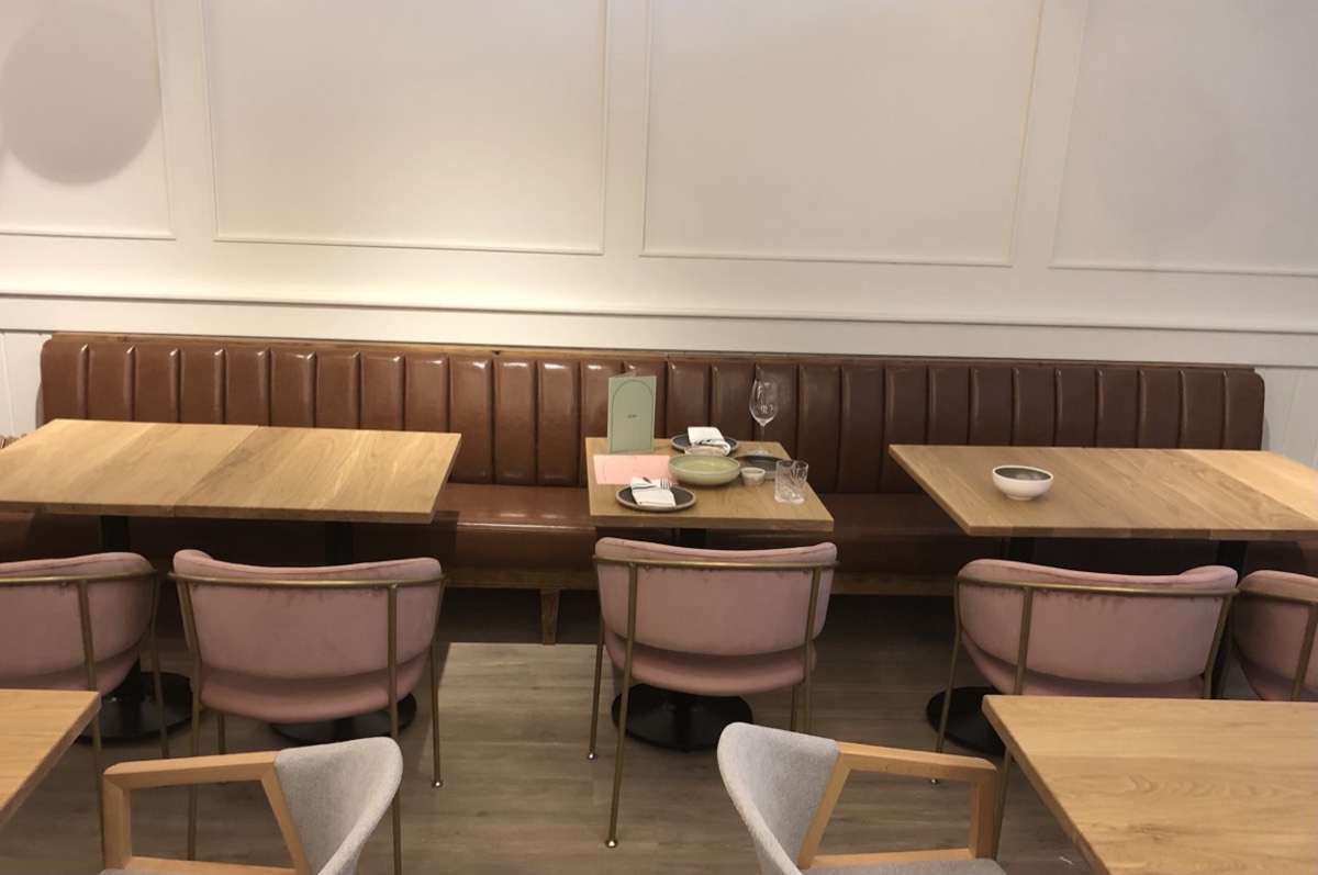 Rust channel-tufted banquette on a panelled white wall with wood tables and pink chairs