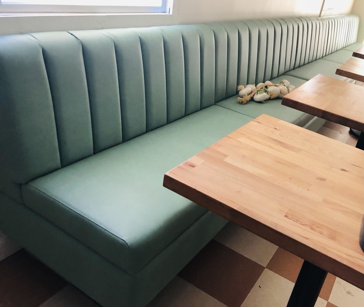 Sage green fluted banquette with butcher block tables above a pink checkerboard tile floor
