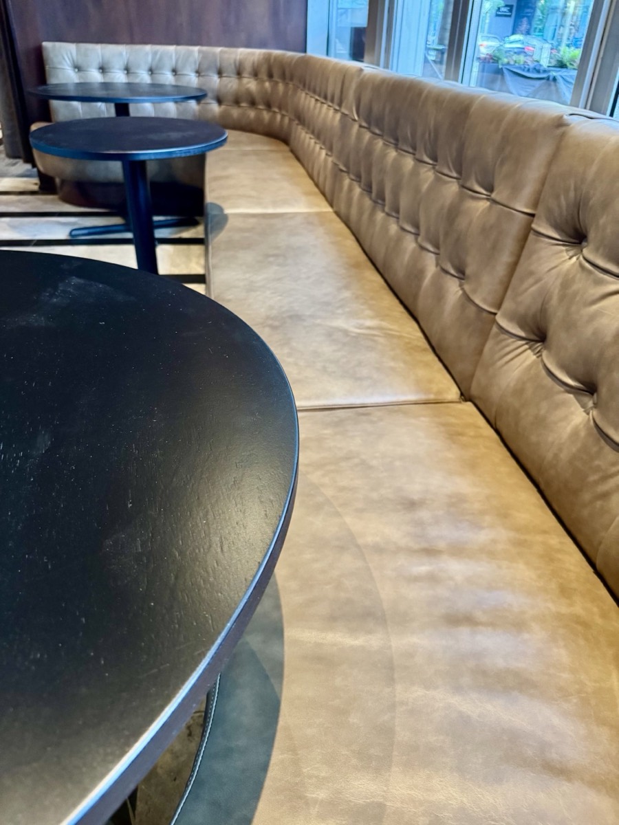Tan leather diamond-tufted banquette running along a wall with round black bar tables