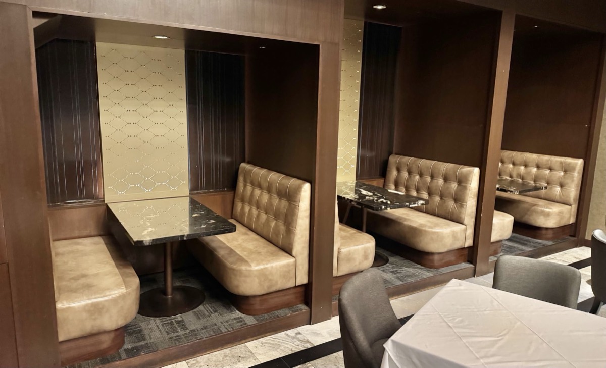 Row of tan tufted booth alcoves in a dim restaurant with a white draped table nearby