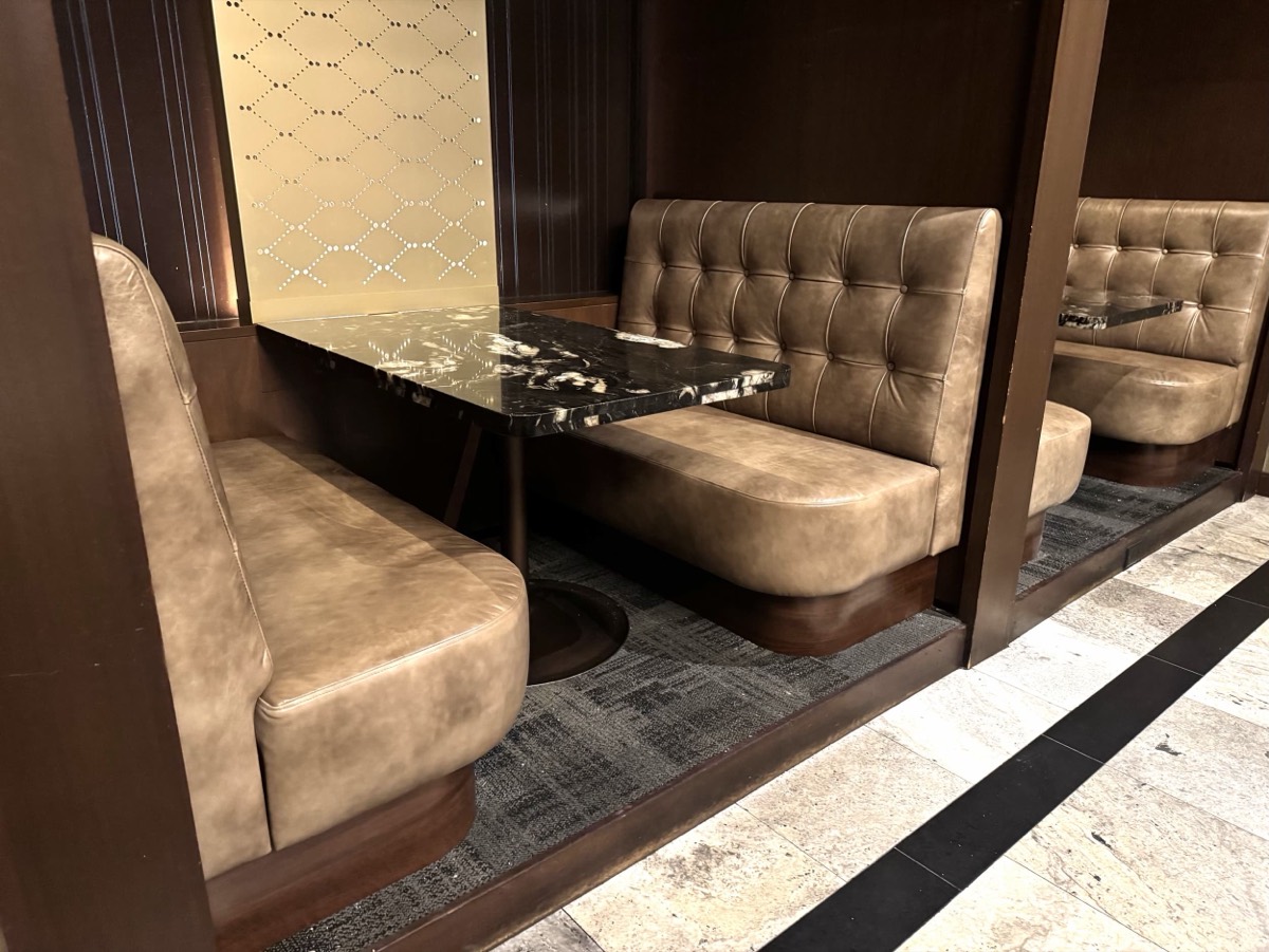 Tan tufted leather booths set inside wood framed alcoves with marble tables and mirrored panels