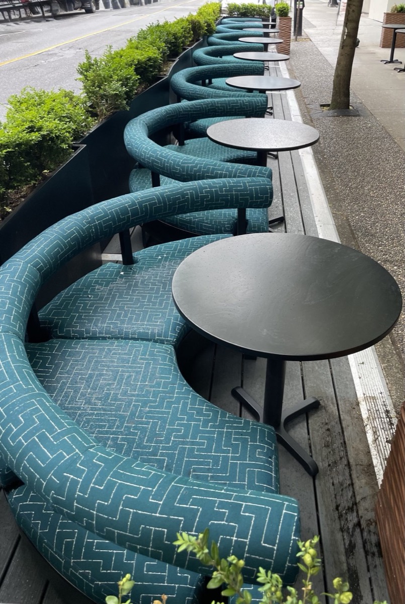 Teal patterned curved outdoor banquettes with round black tables on a sidewalk patio platform