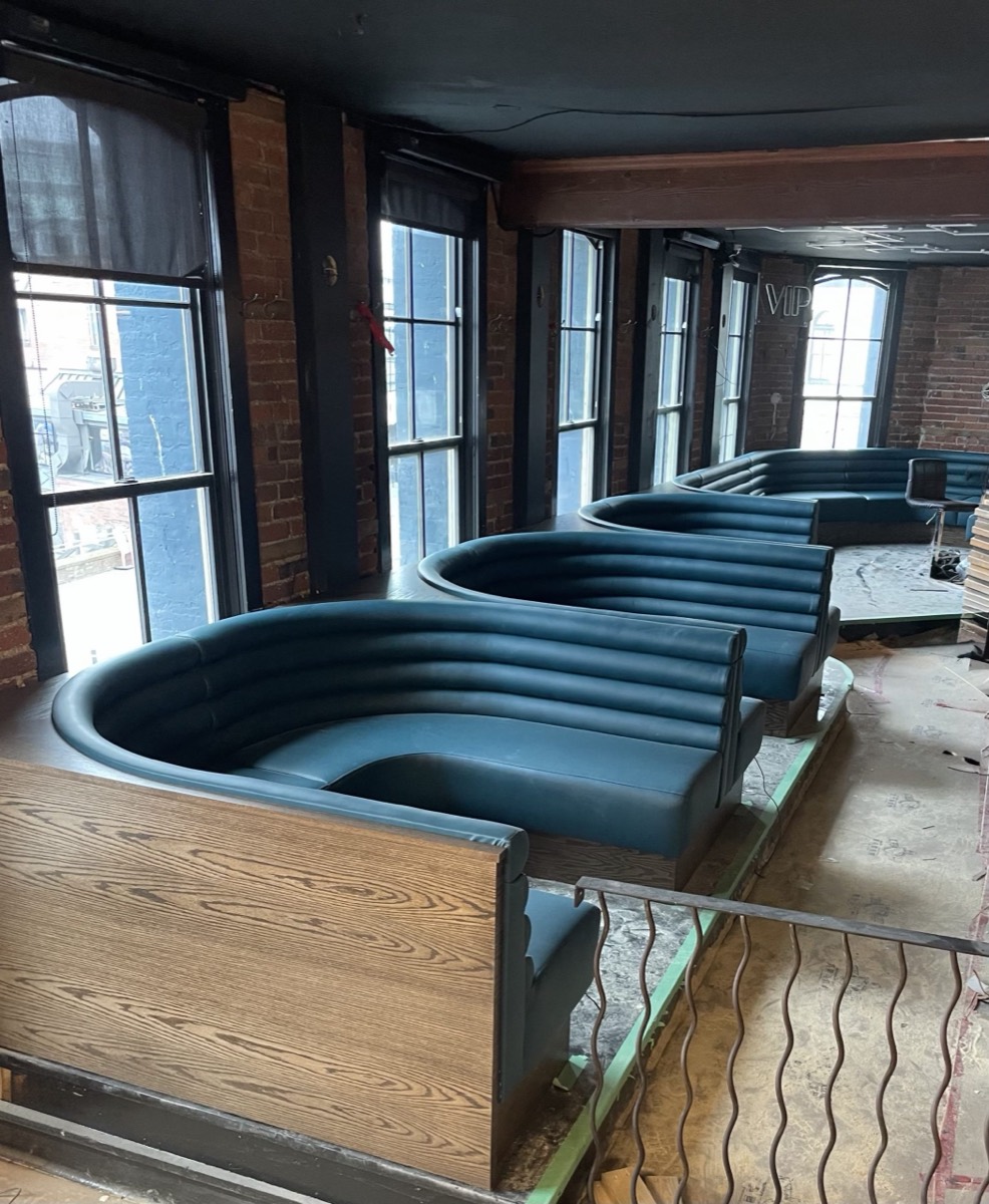 Dark teal horseshoe booths on wood platforms in a brick walled space still under construction