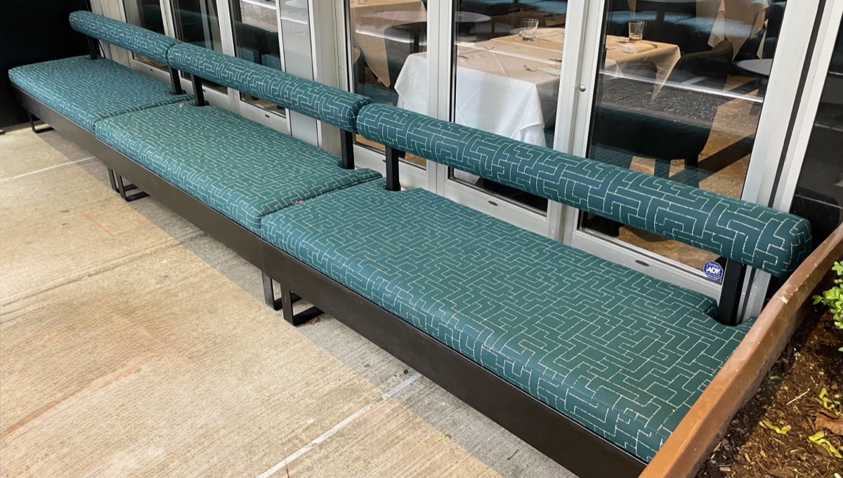Teal patterned outdoor bench seating with round bolster backrests on a concrete patio